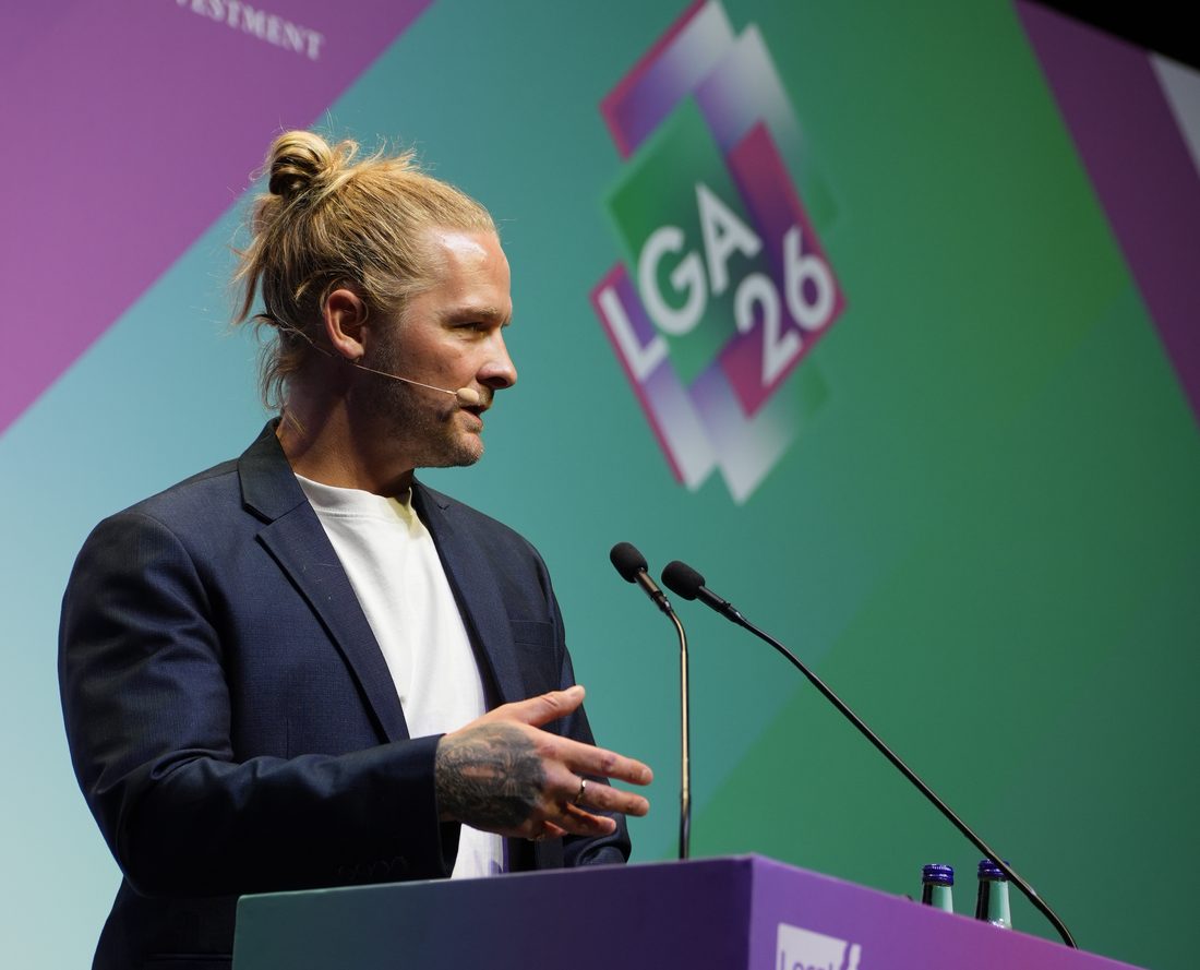Luke Rodgers speaking at the LGA conference, with the LGA 26 logo behind him